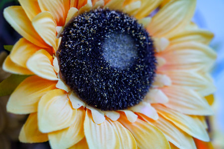 A vivid artificial sunflower features bright yellow petals radiating from a prominent dark brown center. The flower's intricate details highlight its realistic design, perfect for decoration or brightening up a space.の写真素材