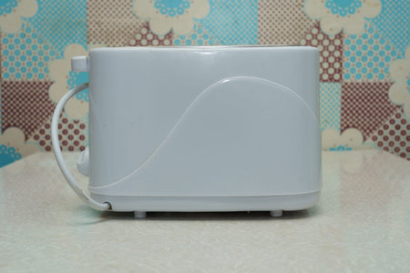 A white toaster sits on a light kitchen counter, featuring a colorful patterned backdrop of dots and...