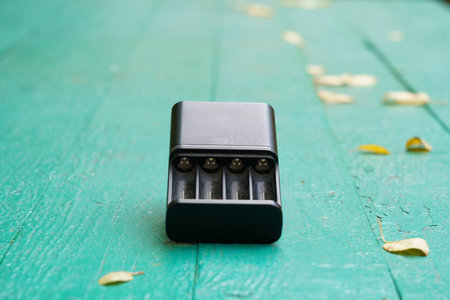 A battery charger is placed on a weathered green wooden table, surrounded by scattered yellow and brown leaves, showing casing autumn vibes.の写真素材