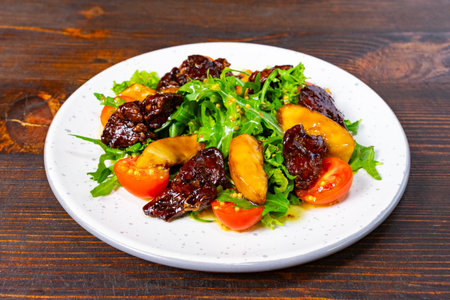 A vibrant salad features fresh arugula, roasted plums, and cherry tomatoes served on a simple plate. The background highlights a wooden table.の写真素材