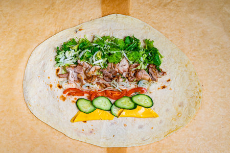 A tortilla wrap is being filled with grilled chicken, fresh vegetables, and cheese. This meal is...