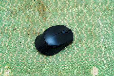A sleek black computer mouse lays on a vibrant green textured surface, illuminated by natural light,...