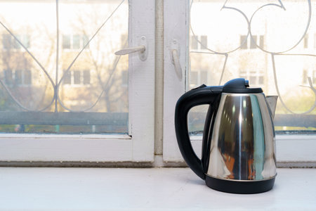 Modern electric kettle on a windowsill with a view of an apartment buildingの写真素材