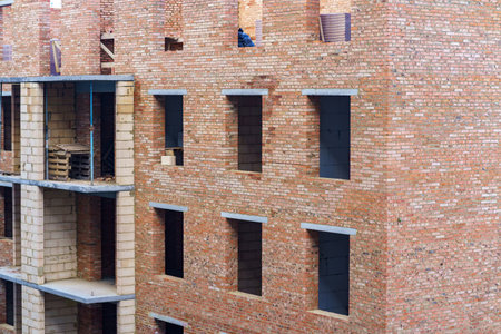 Workers are seen on upper levels of a brick building under construction, with visible window frames and walls nearing completion.の写真素材