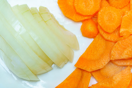 Freshly sliced onions and carrots are neatly arranged on a white cutting board, ready for cooking or salad.の写真素材
