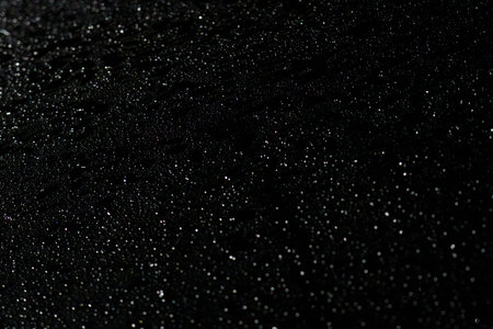 Small water droplets cover a dark surface, reflecting light softly, creating a serene and tranquil...