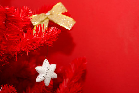 A bright red Christmas tree features a white star ornament and a gold ribbon against a matching red...