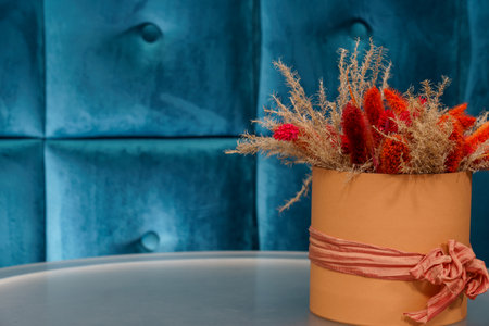 A vase holds colorful dried flowers placed on a round table beside a blue tufted wall.の写真素材