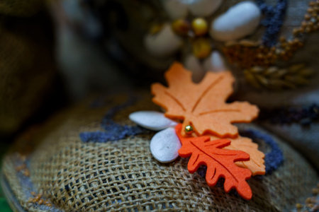 Orange paper leaves and natural objects rest on a textured fabric surface. The scene shows a focus on craftwork and seasonal decor.の写真素材