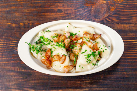 A plate holds dumplings topped with fried meat and fresh herbs, sitting on a wooden table. The food is ready to eat.の写真素材