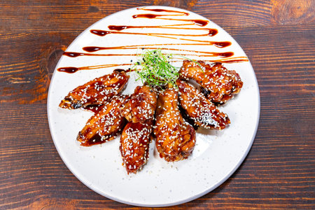 Chicken wings cooked and placed on a white plate with sauce drizzled on top. Garnish is added for...