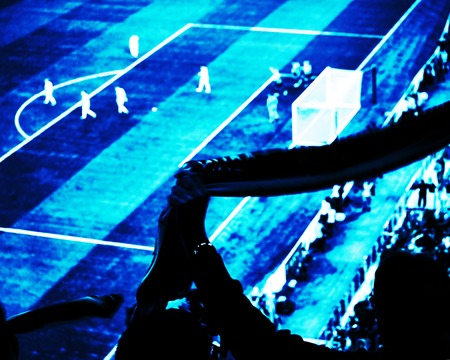 Football fans cheer their soccer team score goal with flags, banners and scarfs at the stadium. Deep blue toned view.の写真素材