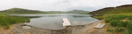 Lake with wooden pier, hill in background. Vacation concept. Russia, lake Shunet.の写真素材