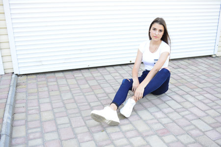 Beautiful young woman wearing jeans, white t-shirt, standing on the street. photo near iron fence.
