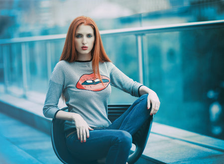 A beautiful girl sits in a chair on the terrace of a cafe against the background of the city. Sexy...