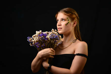 Beautiful young woman face close up portrait in studio on black. bouquet of flowers.の写真素材