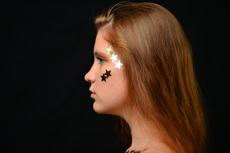 Beautiful young woman face close up portrait in studio on black. various emotions. foil stars glued...