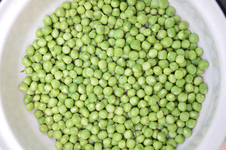 RAW baby peas in small white bowl, on table. Close-up.の写真素材