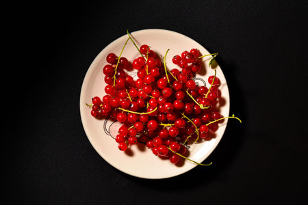 red currant berries on a plate top view. black background with red currantの写真素材