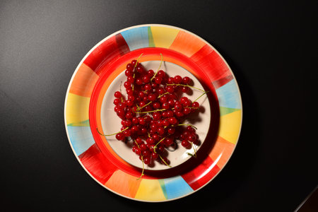 red current berries on a plate top view. black background with red current