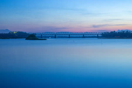 Exposure shot of a river with a railway bridge in the distance, at sunset.の写真素材