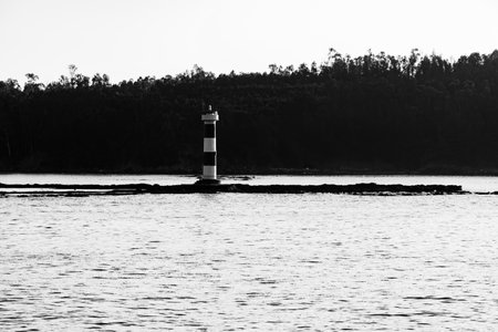 Black and white landscape photo at the mouth of the sea with the lighthouse on the lava rockの写真素材