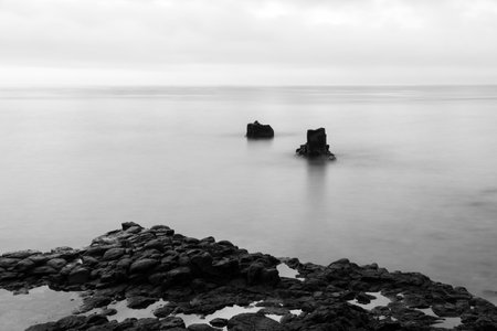 Wide-angle black-and-white exposure of the sea surface with ancient lava rocks protruding above. High contrast image in black and white.の写真素材