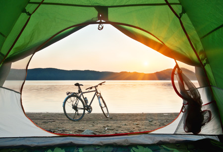 view from the tent to the lake with bicycle on sunsetの写真素材