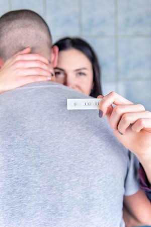 Happy couple hugging with positive pregnancy test in bathroomの写真素材