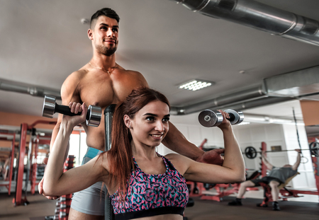 a professional trainer supporting a fit girl exercising with dumbbellsの写真素材