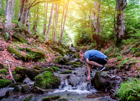 young hiker drinking clear stream water in mountainの写真素材