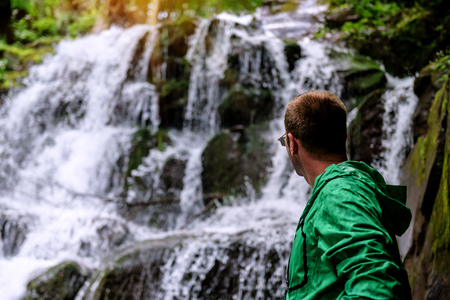 Man in green jacket looking at waterfall Travel Lifestyle adventure concept vacations into the wildの写真素材