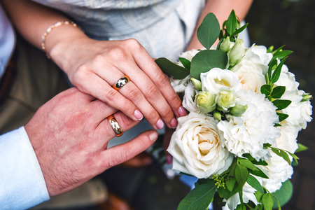 A newly weding couple place their hands on a wedding bouquet showing off their wedding rings.の写真素材