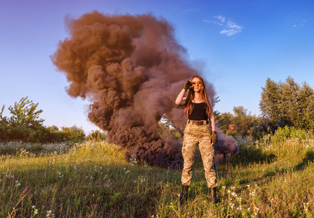military girl on the background of black smoke in the field