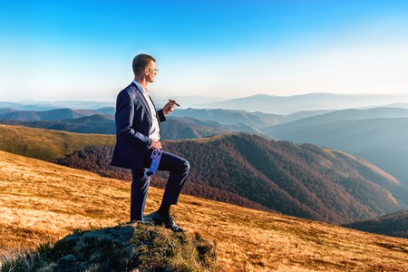 businessman in blue suit with cigar on the top of mountainの写真素材