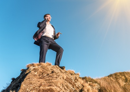 successful man in a business suit on the rock speaks on the smartphoneの写真素材