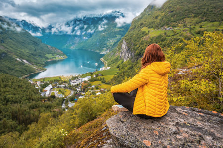 a woman in a yellow down jacket sits over a Norwegian Geiranger fjordの写真素材