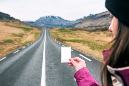 tourist girl holding a printed photo of friends on an empty road in Icelandの写真素材