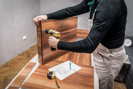 carpenter with electric screwdriver screws the furniture