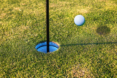 golf ball flying into the hole in green grass