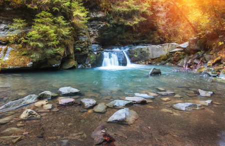 Autumn landscape. Beautiful fall scene on a clear mountain river with small waterfall and rapids, gravel with with colorful rocky bottom and fallen leaves at sunlightの写真素材