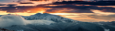 Panoramic view of the winter mountains at sunrise. Landscape with foggy hills. Dramatic cloudy over sky.の写真素材