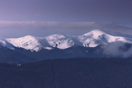 Foggy winter landscape in the mountains. View of forest hills covered by snow and hoarfrost.