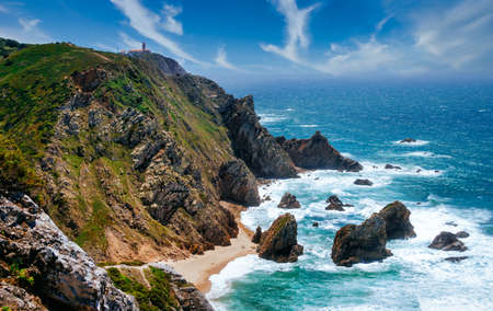 Rocky shore of the Atlantic Ocean. View of high cliffs, foamy waves and sandy beach. Sunny summer seascape. Portuguese riviera. In the area of Cabo da Roca. Portugal.の写真素材