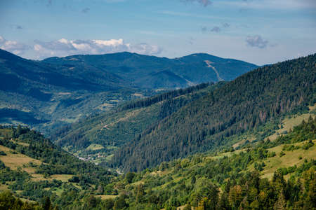 Scenic landscape of the countryside near alpine mountains. View of green hills covered by trees. summer natural background.の写真素材