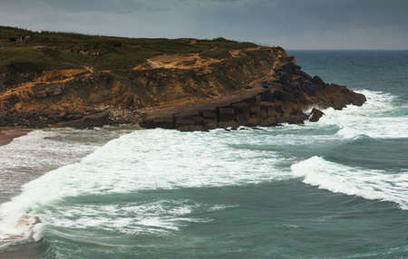 Coastal landscape with dramatic sky over the beach at sunset. View of rocky coast of the Atlantic Ocean with large waves.の写真素材