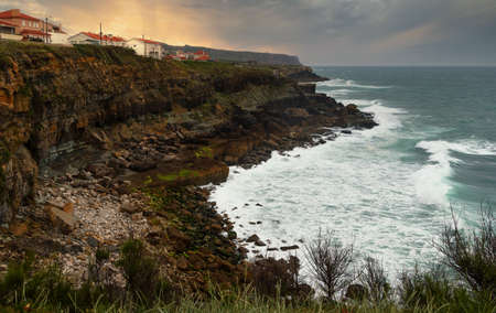 Coastal landscape with dramatic sky over the beach at sunset. View of rocky coast of the Atlantic Ocean with large waves.の写真素材