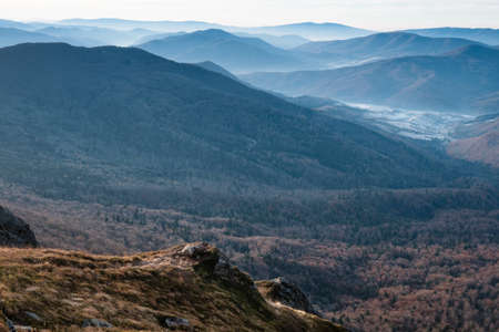 Amazing landscape of mountains layers range at hazy morning. A view of the misty slopes of the mountains in the distance and forest hills in rays of sunlight.の写真素材