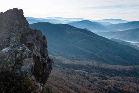 Amazing landscape of mountains layers range at hazy morning. A view of the misty slopes of the mountains in the distance and forest hills in rays of sunlight.の写真素材