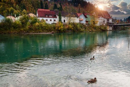 Amazing autumn landscape of a village in the Alps. View of the reflection of the fall colorful forest in the water of the river and of the mountain range in the distance.の写真素材